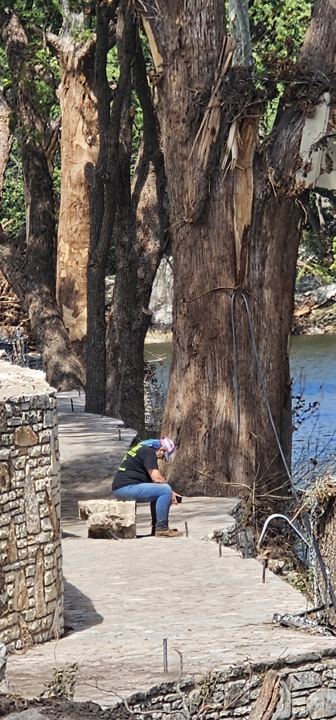 A volunteer rests beside a flood-damaged riverside path
